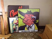 Five vibrant colored Li'l Abner character posters on white plastic sign boards leaning against a wall and a boxed cardboard, featuring Marryin' Sam character prominently in front.