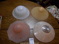 Four vintage glass ceiling light shades arranged on a wooden table showing shape and color variations.