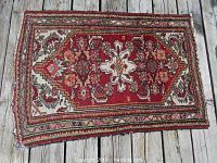 Full view of the older Iranian rug showing rectangular shape and red floral-geometric design on wooden surface.