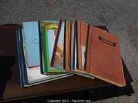 Stack of several scrap books of varying sizes, some spiral bound, some softcover, displayed outdoors on a table.