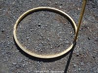 Top-down view of circular, brass base of easel on outdoor surface.