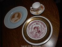 Top-down view of four items on wooden surface: two decorative plates featuring Queen Elizabeth II and King Edward VII with Queen Alexandra, plus a teacup and saucer with Union Jack flags and floral design.