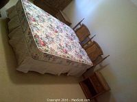 Full view of queen size bed set showing floral mattress and boxspring on a bed frame with wooden headboard and a nightstand visible.