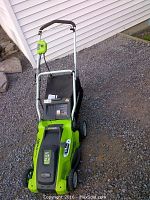 Full view of green electric lawn mower with folded handle, black grass bag attached