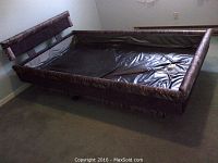 Waterbed frame with padded brown side rails and headboard, black vinyl liner inside.