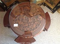 Top view of round carved wood table with glass top and three stools underneath