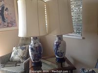 Pair of blue and gold Asian vase lamps on a glass side table, showing full height and design.