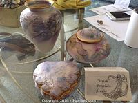 Three porcelain pieces on glass table: vase, oil candle with lid, heart-shaped container with lid, all with purple-pink marbled finish and gold accents