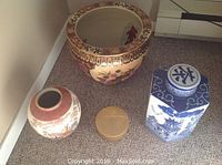 Image showing four Asian decorative items on carpet: one large floral pot with wide ornate rim, one large round floral vase, one hexagonal blue and white urn, and one small gold coaster.