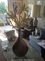 Tall metal vase with artificial white flowers and branches on living room glass table