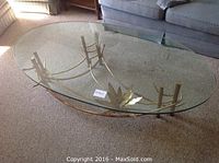 Top view of oval glass table showing clear thick glass and decorative metal base with leaf accents.