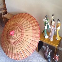 Eight Asian figurines standing on a small gold table beside a large red and gold Chinese umbrella.