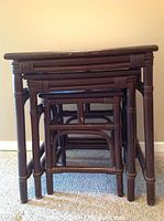 Side view of three dark wood nesting tables stacked inside each other showing wrapped detailing on legs and frames.