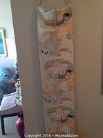 Full view of Obi sash hanging vertically on wall with rope and rod, showing the sash's full length and pattern.