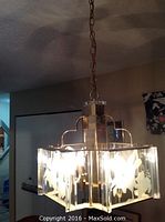 Chandelier hanging from ceiling showing brass frame and etched glass panels depicting floral patterns