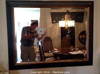 Photo of the black wooden framed mirror with copper accents hung on a wall, reflecting a dining room scene.