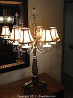 Front view of gold color table lamp with six lit fabric lampshades and glass bead decorations, showing ornate base and crystal finial top.