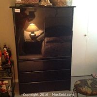 Closed view of tall black lacquer cabinet with three large lower drawers and two-door upper section.