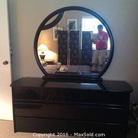 Front view of black lacquer dresser with round mirror mounted or resting on it, room background visible.