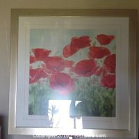 Framed print showing red poppy flowers with a natural wood colored frame and visible double matting.