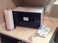 Panasonic microwave oven, paper towel stand with paper towels, and white corded telephone on kitchen counter.
