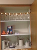 Shelf with eight clear glasses with gold rims on top shelf, citrus juicer and kitchen appliances on lower shelves