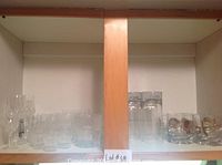 Upper cupboard shelves showing an assortment of clear glassware including wine glasses, tumblers, tall glasses, and glass jars.