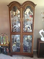 Front view of curio cabinet with display items removed to show glass doors, arched top, gold leaf decoration.