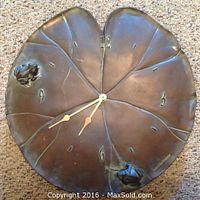 Top view of the bronze-colored lily pad outdoor wall clock showing the clock face, numbers, and frog figures on the clock surface.