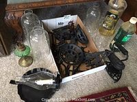Cast iron decorative pieces, trivet, sad irons, hook, and oil lamp parts alongside glass lamp shades and an oil bottle.