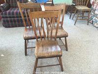 Front view of three wooden arrow back chairs showing aged wear on seats and backs.