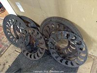 Five dark metal grates stacked upright against a wall, showing the cast iron construction with decorative cutouts and varying diameters.