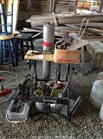 Photo showing the Tut-E-Nuf folding tool bench loaded with assorted tools, a large roll of vapor barrier wrap, and a box of nails and metal parts.