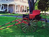 Side view showing red tufted seat, black body, red shafts, wooden wheels with metal rims