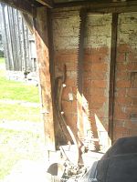 Large cross saw with serrated blade and wooden handles leaning against brick wall