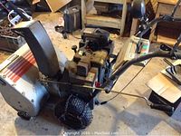 Side angle of the snow blower showing the engine, wheels, and handle.