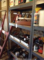 View of metal shelving with red tool case, assorted small fittings, spray can, and oil containers.