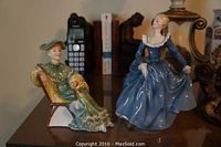 Front view of two Royal Doulton figurines with a cordless phone and books in the background