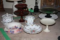 Full view of assorted china and servingware including pedestal dishes, lidded jars, and lacquerware on carpet.