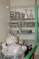 Photo showing shelves with etched glassware including bud vase, silver-rimmed highball glasses, pressed tumblers and glass carafes