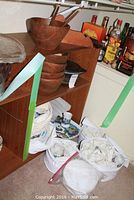 Shelving unit holding wooden bowls, ceramic plates with floral patterns, and wrapped items in bags beneath shelf.