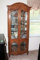 Front view of the curio cabinet with various dishware displayed inside the upper section behind bevelled glass doors.