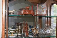 Full view of the glass shelf with various decorative and collectible items including carved wooden box, ceramic figures, vase, and Mikasa clock.