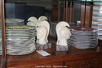 Two stacks of plates flanking pair of alabaster helmet bookends on wooden surface
