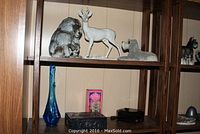 Wide shot of two shelves showing figurines, glass vase and decorative boxes