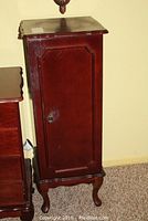 Jewelry cabinet closed showing dark wood finish, raised panel door, and carved legs.