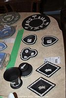 Overview of black Wedgwood jasperware items on table including large round plate, small dishes of various shapes with white relief classical figures and borders