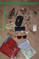 Photo of assorted eyeglasses, magnifier glasses with case, sunglasses, scissors, and an instruction sheet on carpeted surface.
