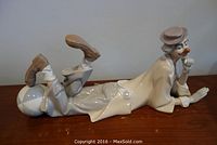 Photo showing side view of Lladro porcelain clown figurine, lying on stomach with legs raised and balanced on a colored ball, detailed face and clothing visible.