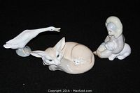 Group view of three Lladro porcelain figurines: Eskimo child figurine, goose figurine, and fox figurine with a kitten nestled on its side.